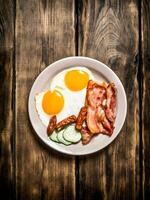 plate of fried eggs, bacon , cucumber and smoked sausages. photo