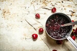 Cherry jam in a saucepan on the old fabric. photo