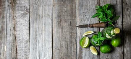 Cocktail in glass and bottle , also mint and limes on a wooden table . Free space for text. photo