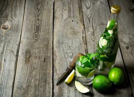 Cocktail in glass and bottle , also mint and limes on a wooden table . Free space for text. photo