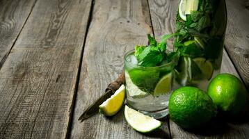 Cocktail in glass and bottle , also mint and limes on a wooden table . Free space for text. photo