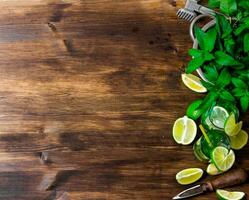 The ingredients for the cocktail - limes, rum, mint leaves, ice cubes on wooden table. Free space for text. photo