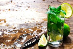 Glass of cool cocktail , ice, knife and slices of lime on a wooden table. photo