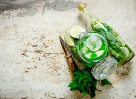 The cocktail in the jar, the bottle with ice cubes, lime, mint leaves and rum . photo