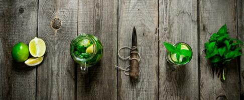 The ingredients for the cocktail - mint leaves, limes, rum and a knife for citrus fruits on the wooden table. photo