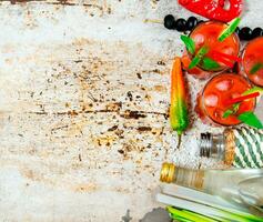 Cocktail made of tomatoes, vodka, ice, lime, pepper , salt and snack with celery and black olives on rustic background . photo