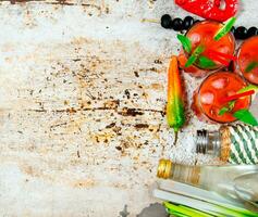 Cocktail made of tomatoes, vodka, ice, lime, pepper , salt and snack with celery and black olives on rustic background . photo