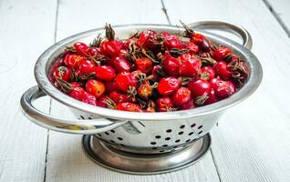 Rosehips in metal bowl on wooden table. photo