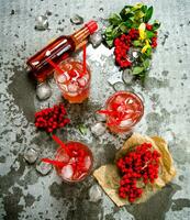 Three cocktails with ice.  Ingredients - liquor, berries, juice, and clean water on the stone table. photo