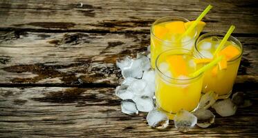 Three cocktails from fresh oranges with ice and straw on wooden background . Free space for text. photo