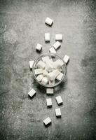 Refined sugar in a glass saucer. On stone background. photo