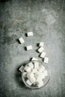 Refined sugar in a glass saucer. On stone background. photo