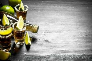 bottle of tequila with shot glasses, fresh lime and salt. photo