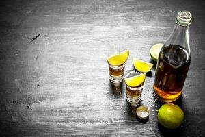 bottle of tequila with shot glasses, fresh lime and salt. photo