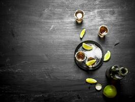 bottle of tequila with shot glasses, fresh lime and salt. photo