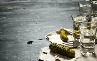 Glasses with vodka and pickled cucumbers on the old fabric. photo