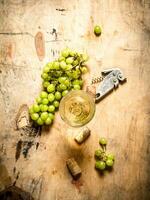 vaso de blanco vino con uvas y un sacacorchos. foto