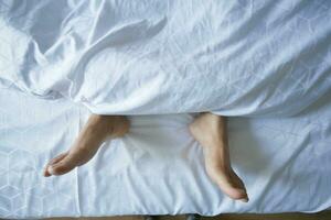 young Woman lying with bare feet in bed, photo