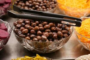 slices black olives with spoon in a bowl , photo
