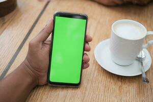 sosteniendo una cpu de café y usando un teléfono inteligente con pantalla verde foto