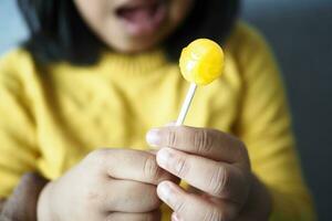 child is licking yellow color lollipop candy on stick, photo