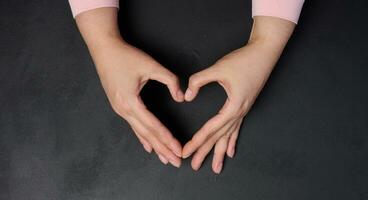 Two female hands folded in the shape of a heart on a black background photo