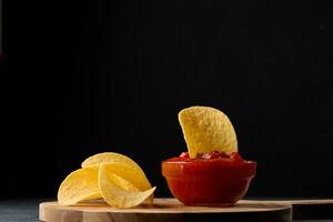 Potato chips in a wooden bowl and a bowl of sauce on a black table, snack photo