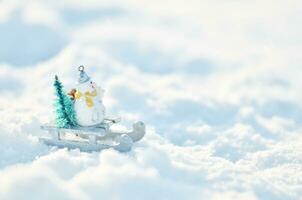 Snowman in a sleigh with a Christmas tree in snowdrifts. Winter season background. photo
