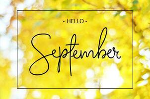 Hello september greeting card on background autumn leaves with bokeh and glare of light. photo