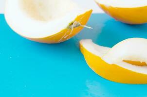 Yellow honeydew melon half with seeds and slices on blue background. - Image photo