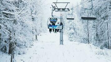 Pamporovo, Bulgaria, January 2023 Skiers wearing protective equipment riding ski lift to reach frosty mountain top slope surrounded by pine trees during winter holiday season. Extreme sports video