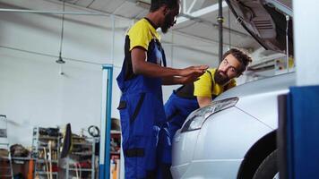 Trained technicians in auto repair shop working together on fixing car, discussing best options. Professional and colleague collaborating on servicing broken vehicle, checking for defective components video