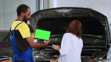 afrikanisch amerikanisch Mechaniker mit Grün Bildschirm Laptop zu Show Frau beschädigt Komponenten gefunden im ihr Wagen. Handwerker mit Attrappe, Lehrmodell, Simulation Gerät zu Hilfe Klient visualisieren Reparaturen zu Sein erledigt zu Fahrzeug video