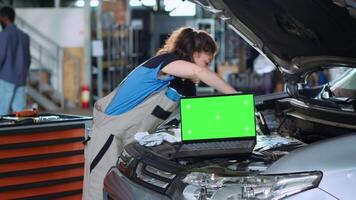 Chroma key laptop in garage facility sitting on malfunctioning car. Green screen device in auto repair shop next to mechanic cleaning vehicle inside engine compartment after fixing it video