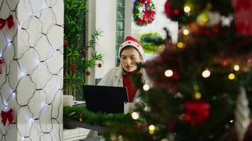 Zoom in shot on focused employee working on overdue project during Christmas season in festive decorated office. Worker in multicultural workplace adorn with red xmas garlands and bows video