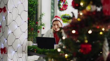 enfocar en Disparo en enfocado empleado trabajando en atrasado proyecto durante Navidad temporada en festivo decorado oficina. trabajador en multicultural lugar de trabajo adornar con rojo Navidad guirnaldas y arcos video