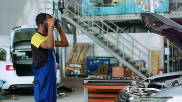 africain américain mécanicien dans voiture un service en utilisant virtuel réalité des lunettes de protection à simuler voiture réaction à route conditions après fixation il. dépanneur portant haute technologie vr casque à tester véhicule moteur video