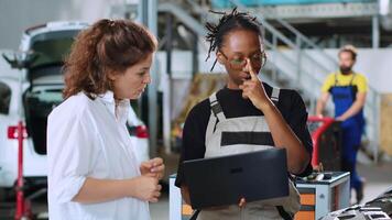 Meticulous technician in car service using laptop to calculate repairments invoice for client after fixing damages. Trained expert using device to inform woman of final costs after servicing vehicle video