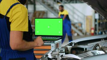 Licensed repairman using green screen laptop in car service to order new parts for busted vehicle. Close up shot of professional using chroma key device to look on internet for replacing components video