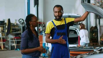 qualifié auto réparation magasin mécanicien montrant client défauts a trouvé à l'intérieur voiture après inspection. africain américain professionnel récit femme à propos cassé radiateur a trouvé dans sa véhicule video