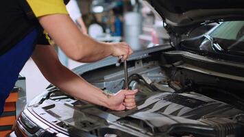 Certified mechanic in car service uses wrench to tighten bolts after fixing vehicle parts. Repair shop employee utilizing professional tools to make sure automobile is properly working, close up video