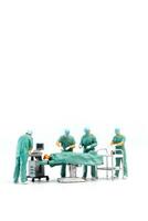 Miniature Doctor performing surgery on patient on white background photo