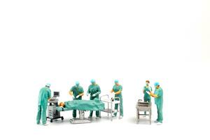 Miniature Doctor performing surgery on patient on white background photo