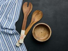 Empty bowl and wooden spoons on a black table, top view photo