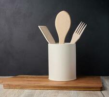 Wooden spoons and forks in a stand on a black background, kitchen utensils photo