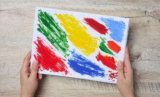 Female hands holding a white sheet of paper with strokes of acrylic multi-colored paint, top view photo