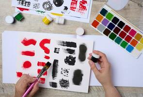 Set of watercolor paints, brushes and paper with different strokes and colors. Female hands holding a brush photo