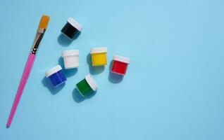 Plastic jars with multi-colored gouache on a blue background, copy space photo