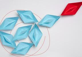 Group of blue paper boats heading in one direction and one red one heading in the opposite direction. photo