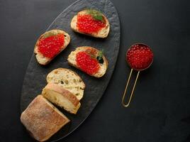 rojo caviar en rebanadas de blanco trigo un pan en un negro mesa, concepto de lujo y gastrónomo cocina foto